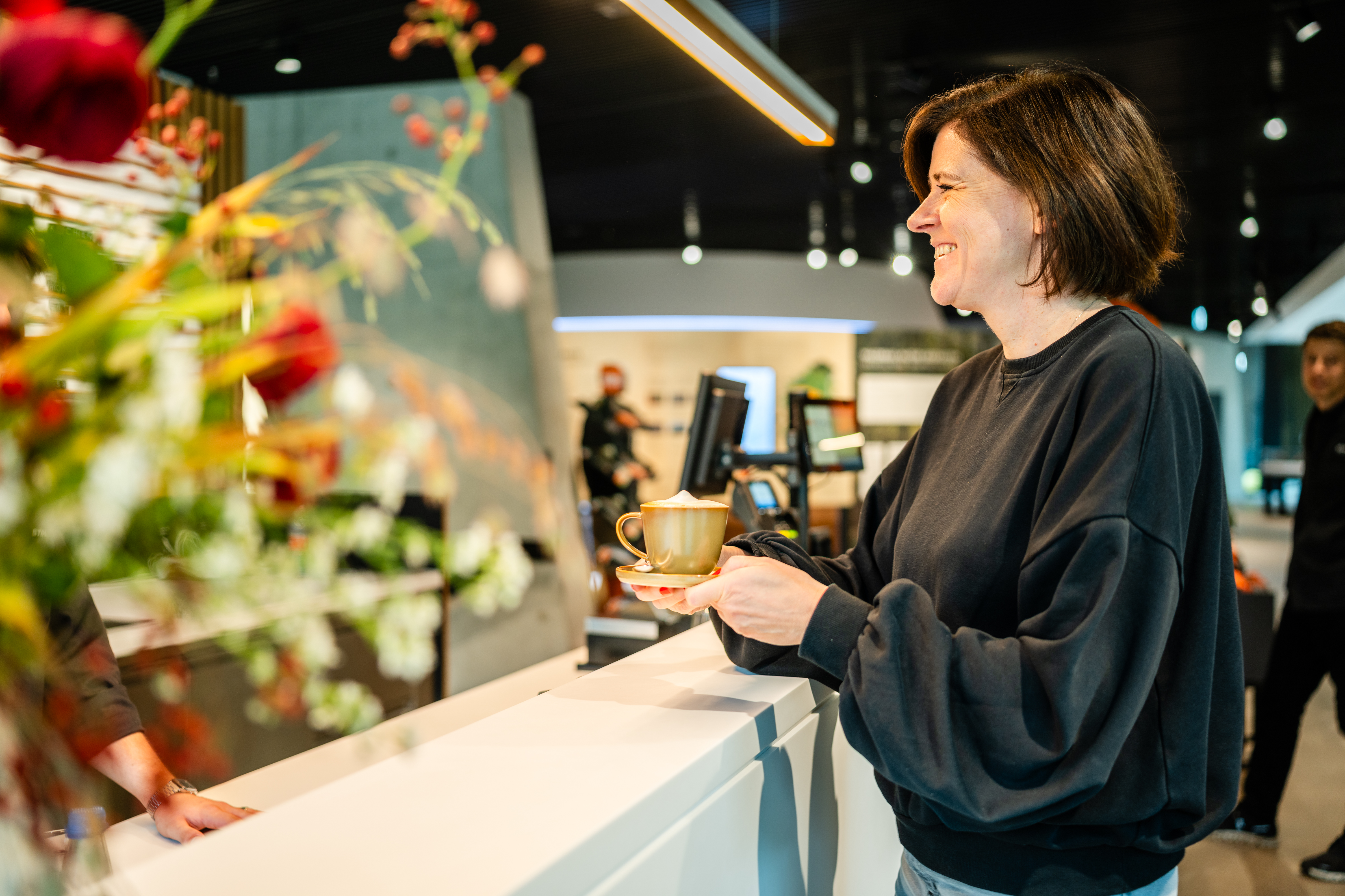 Eine Frau hält lächelnd einen Kaffe in der Hand.